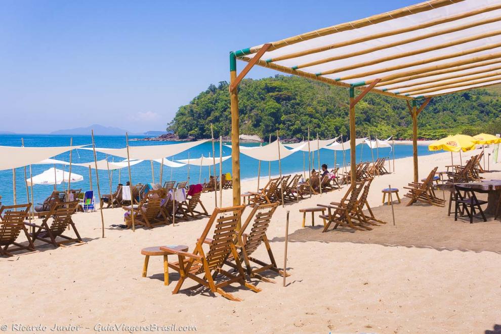 Imagem de lindas cadeiras de madeira com guarda sol estiloso nas areias da Praia de Prumirim em Ubatuba.